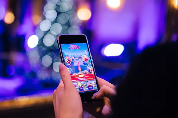 Uma jovem relaxando com o celular enquanto elementos dinâmicos de cassino flutuam ao seu redor, ilustrando a experiência móvel fluida oferecida pelo app 83BET.